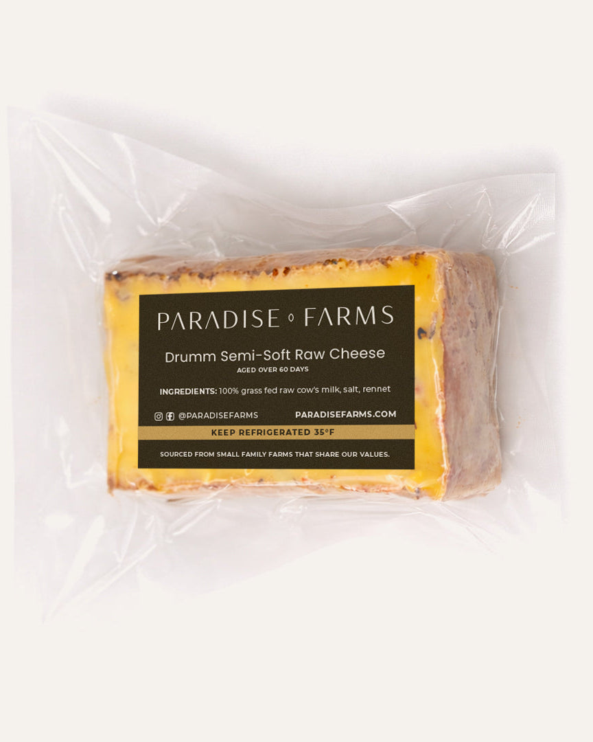 Block of Paradise Farms Drumm Semi-Soft Raw Cheese wrapped in plastic on a white background