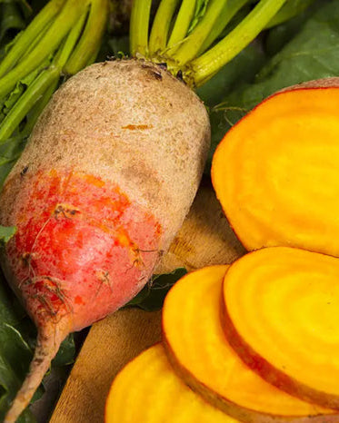 A whole golden beet with leafy greens attached, alongside sliced beets displaying the golden color.