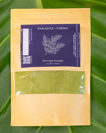 Packaging of Moringa Powder from Paradise Farms on a green leaf background