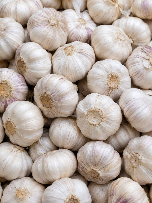 A close-up pile of whole garlic bulbs with pale ivory to off-white papery skins and subtle purple streaks, filling the frame.